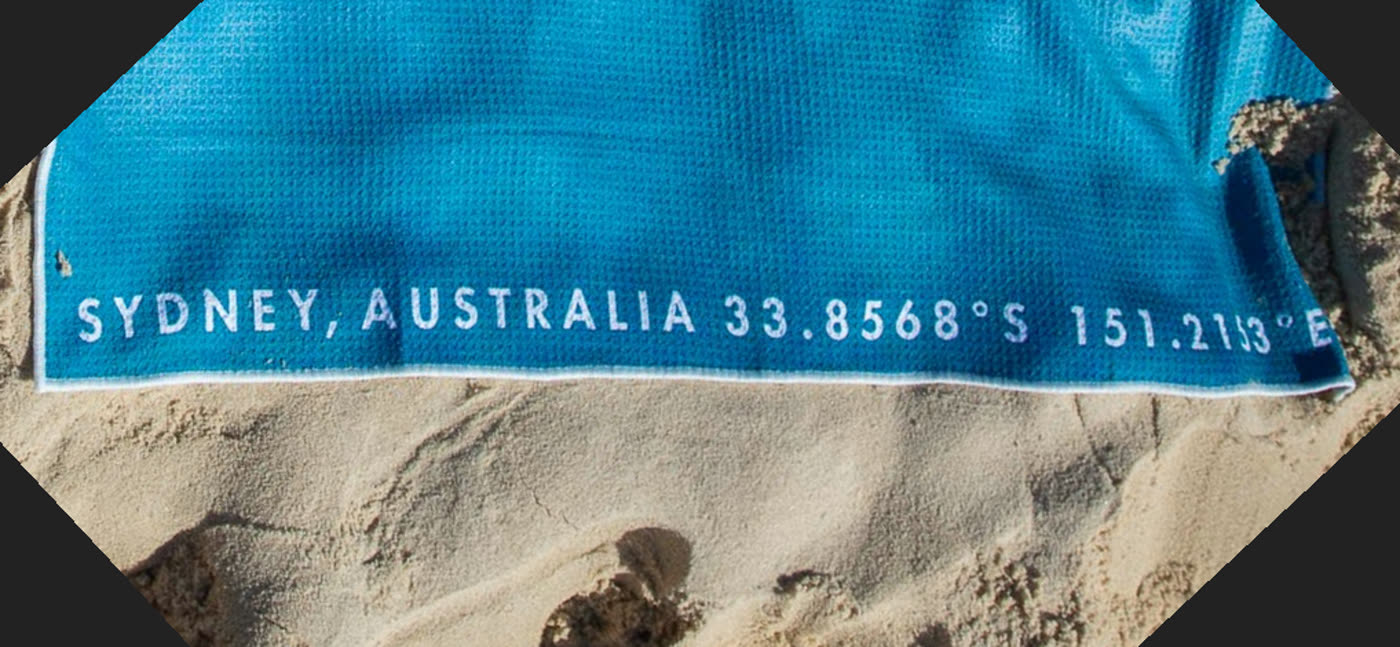 Close-up of the printed GPS coordinates along the edge of a beach towel on the sand