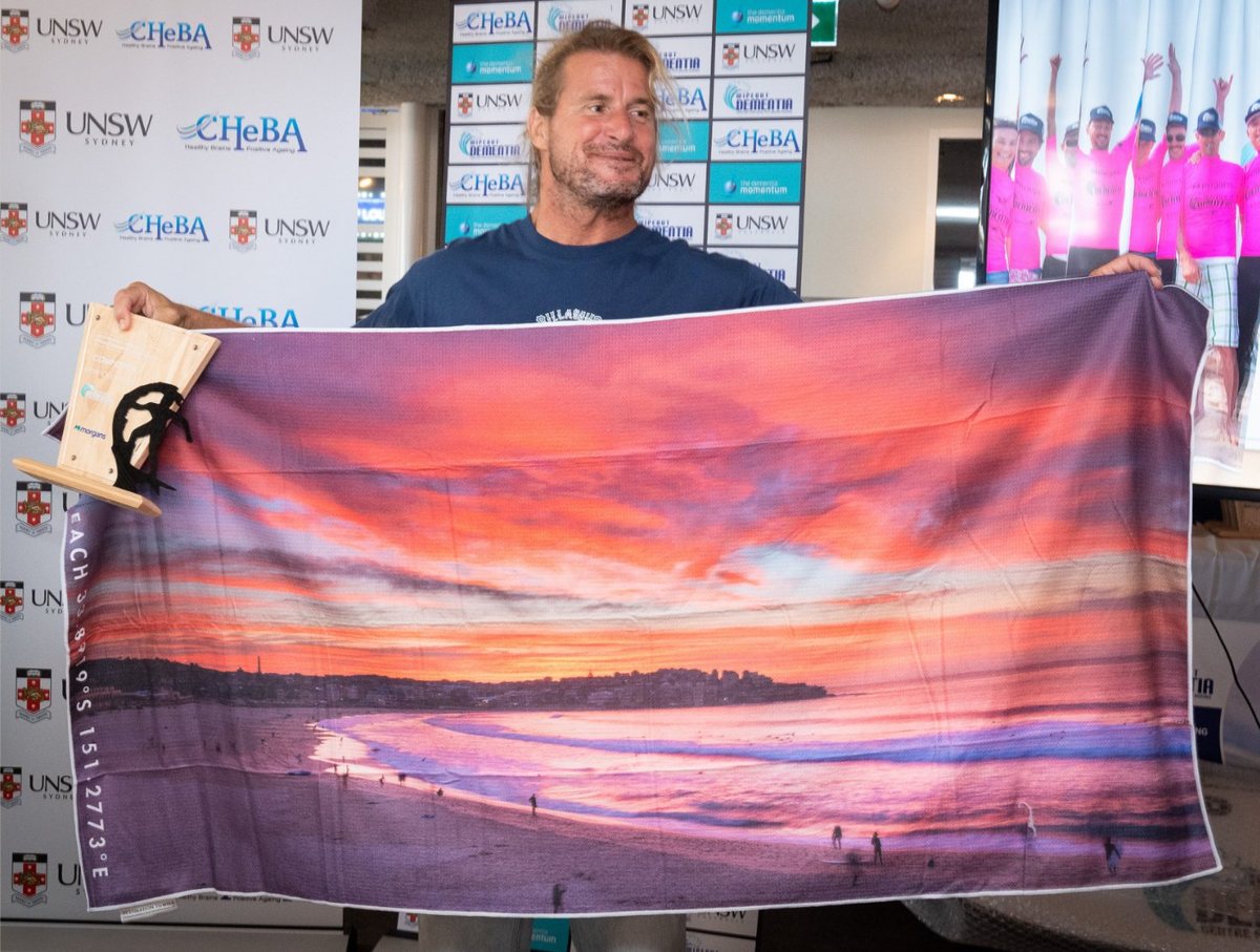 Mark Occy Occhilupo holding a Destination Label Bondi sunrise beach towel at the Wipeout Dementia event